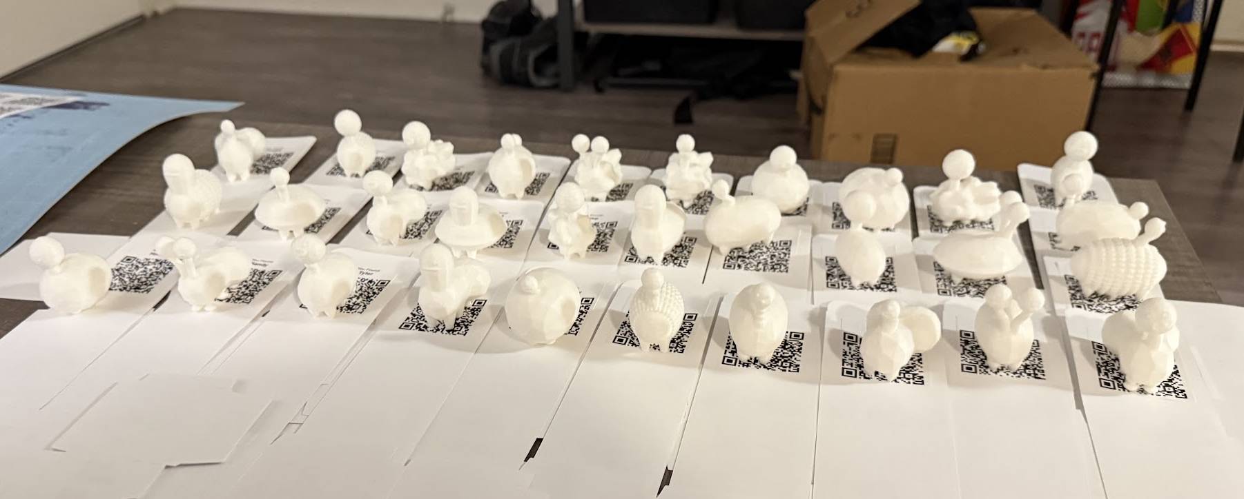 A collection of 3D-printed creature toys, 3 rows of 10 creatures, displayed on a wooden coffee table. The creatures are sitting on top of paper boxes with QR codes printed on them.